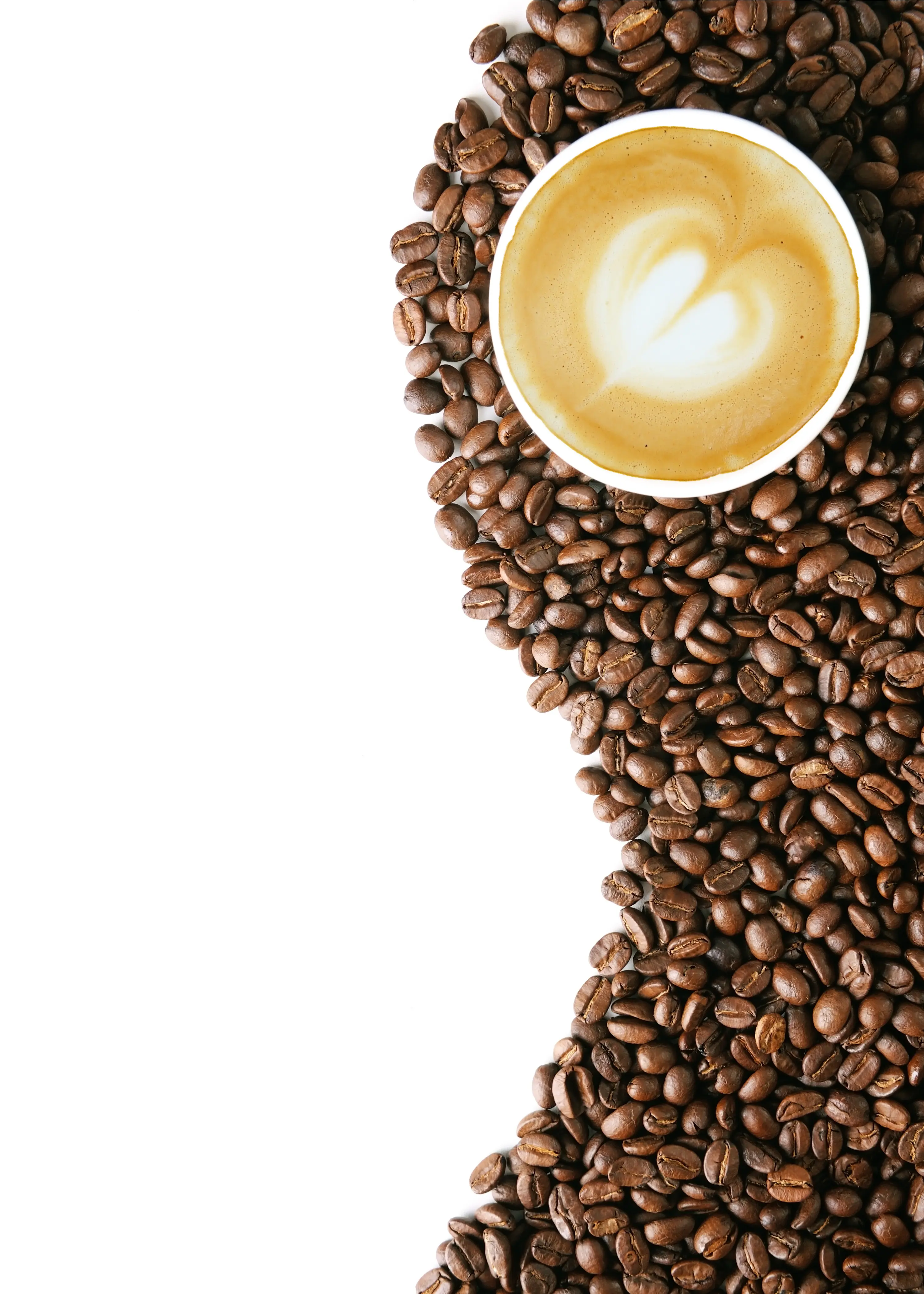 Coffee beans on a bright white table top with a cup of coffee with a white foam heart in the center. 