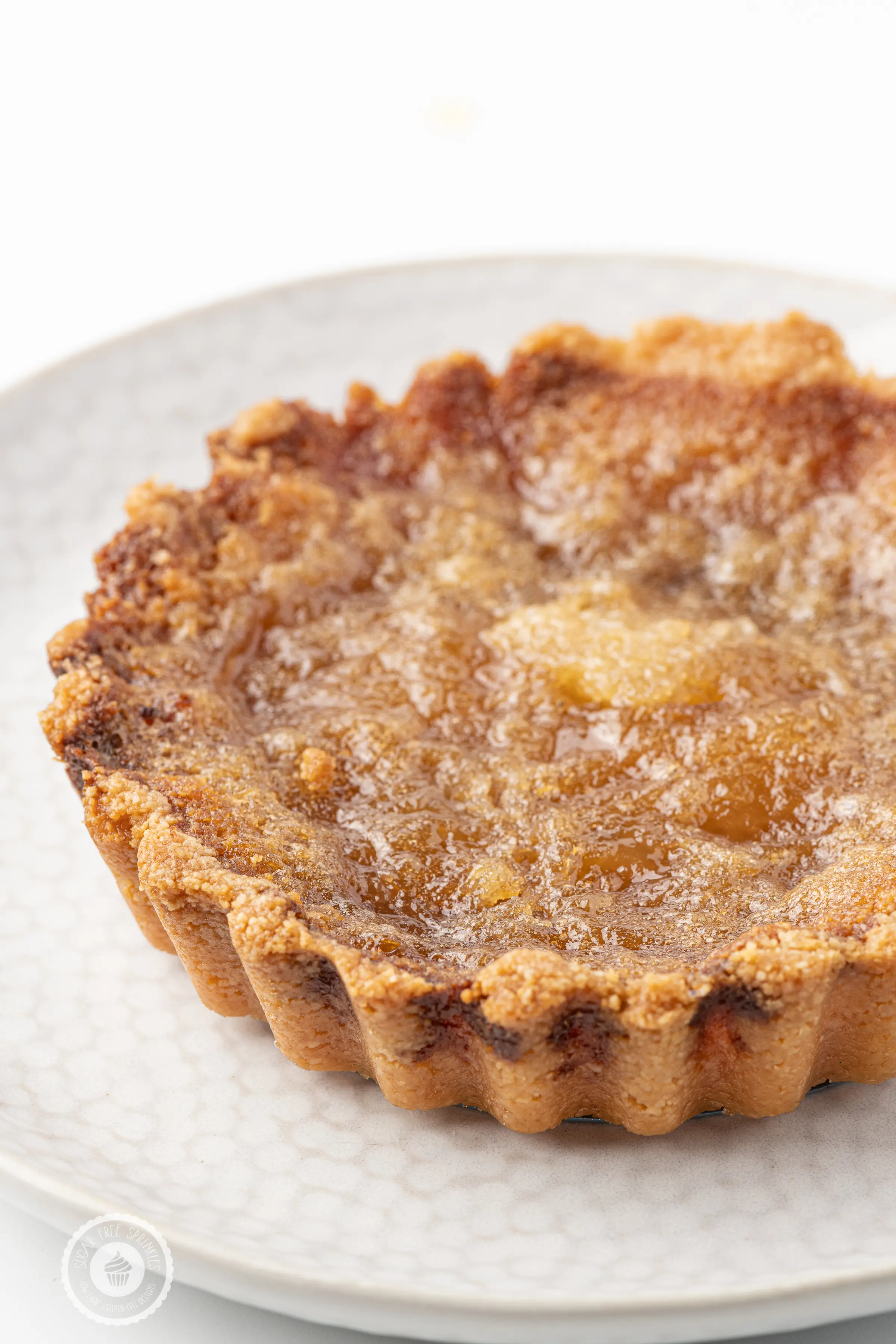Golden brown sugar-free butter tart on a white plate against a bright white background. 