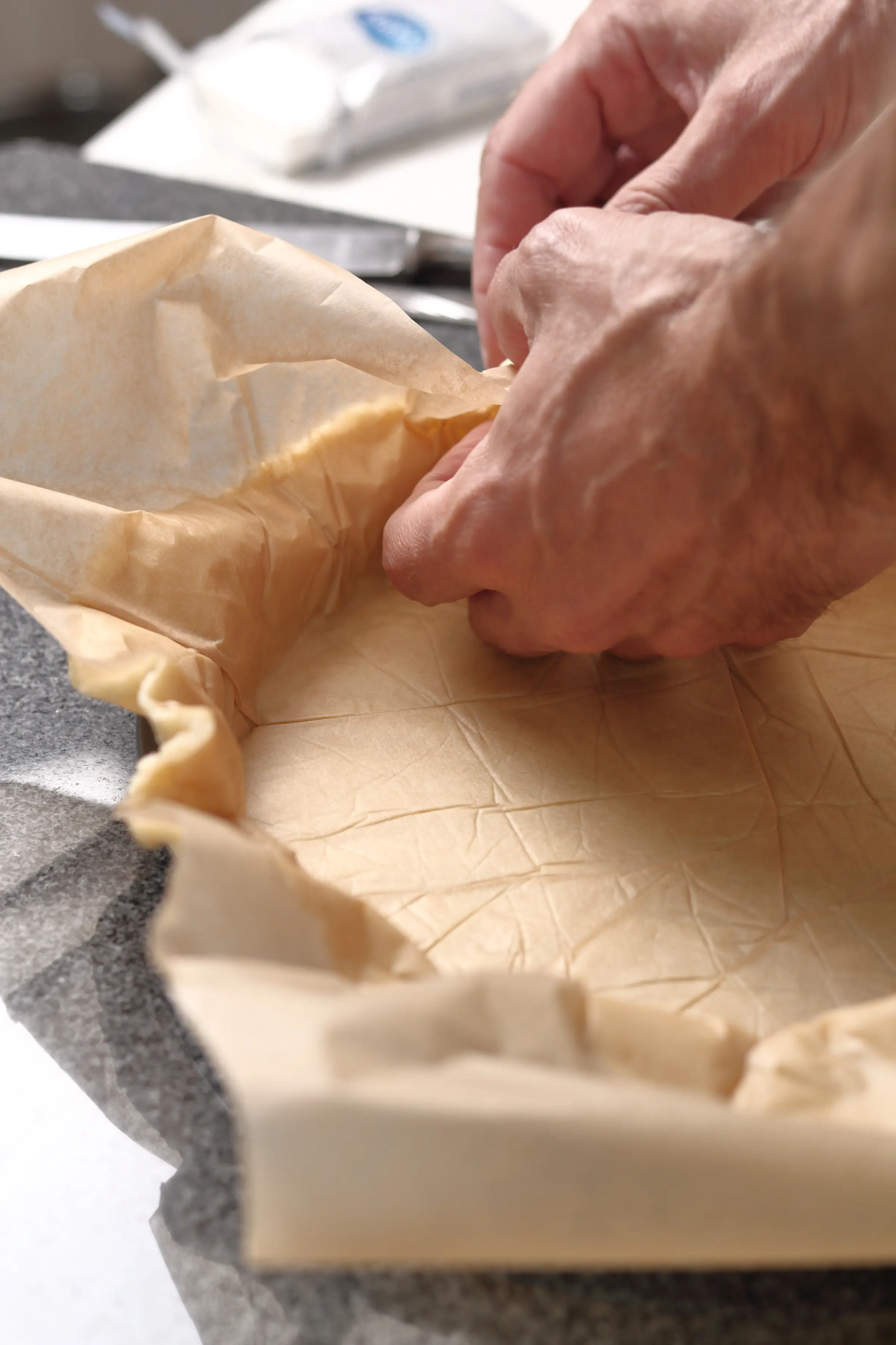 A pie crust being pushed into a pie tart shell with parchment paper. 