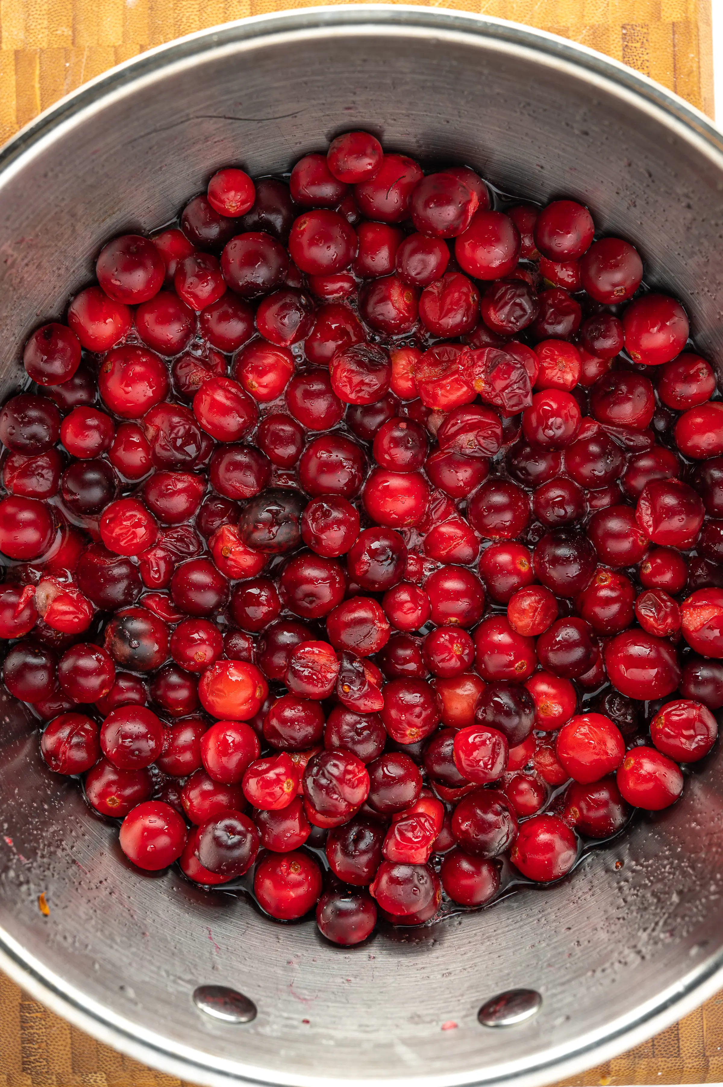 A pot of red ripe cranberries cooking in sugar-free syrup.  A few of the berries have cracked.