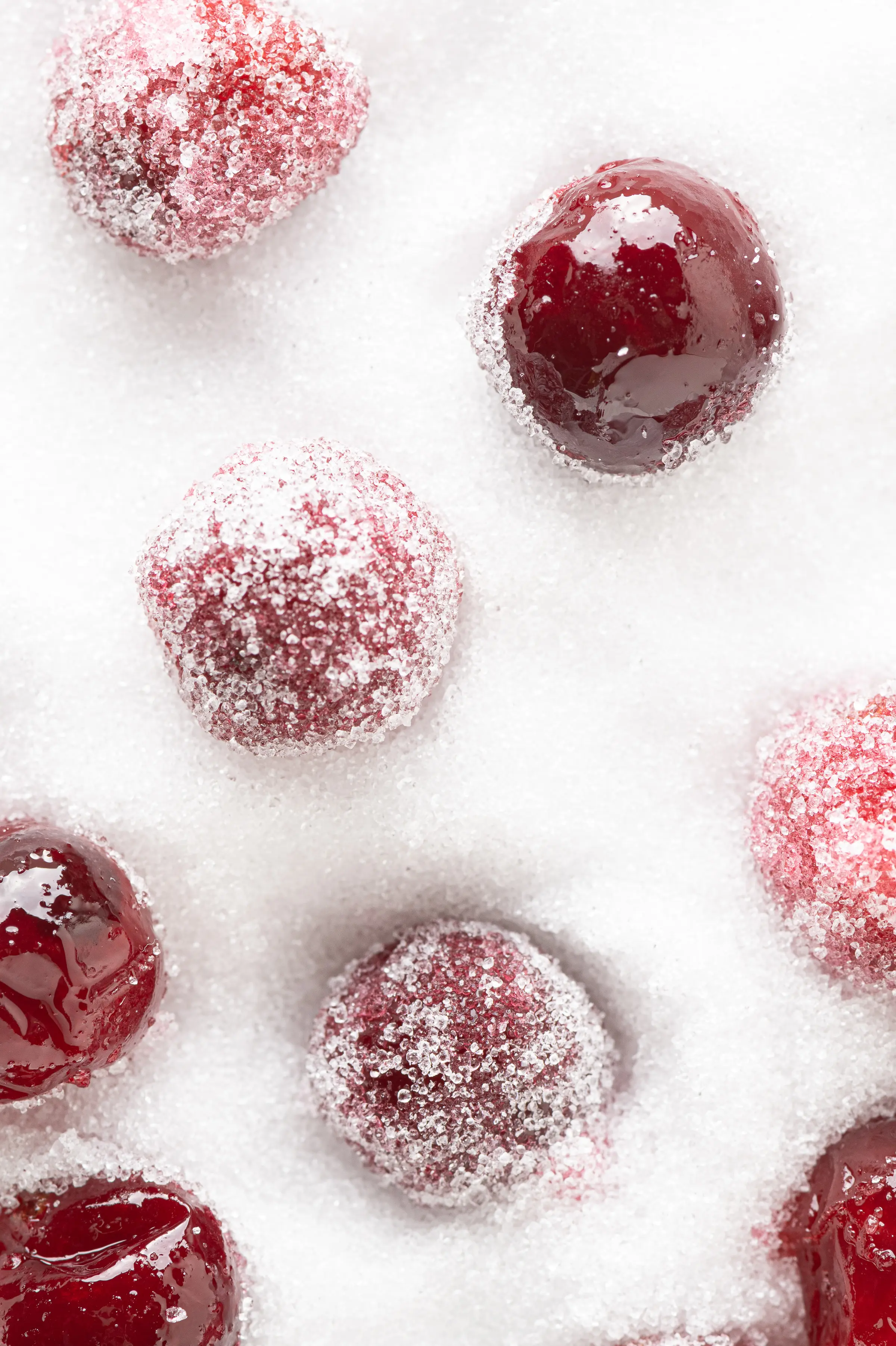A few coated and uncoated sugar-free candied cranberries sitting in a dish of granular sweetener. 