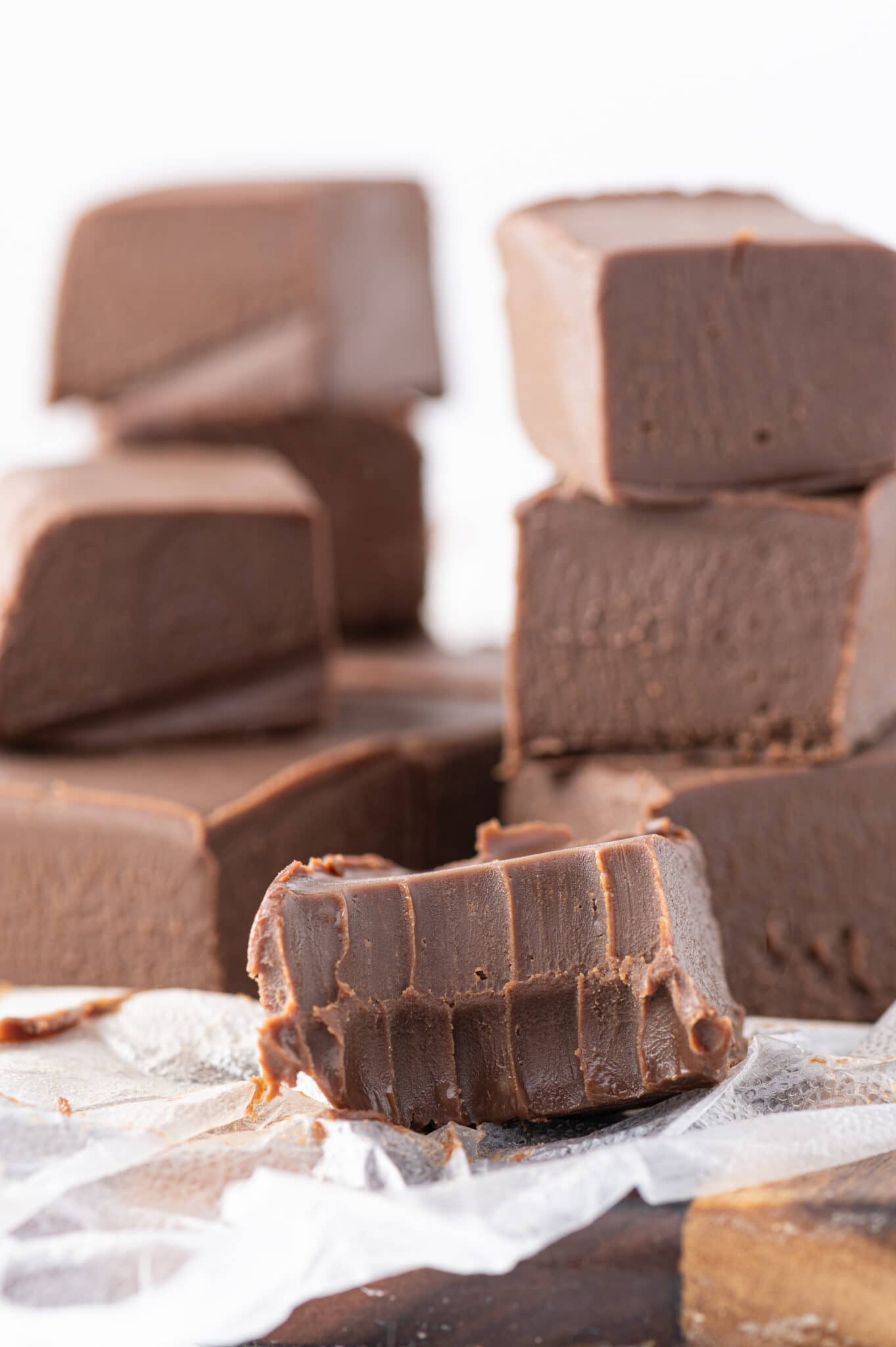 A piece of keto fudge in the foreground with a bite taken from it, with more fudge cubes from this recipe stacked in the background.