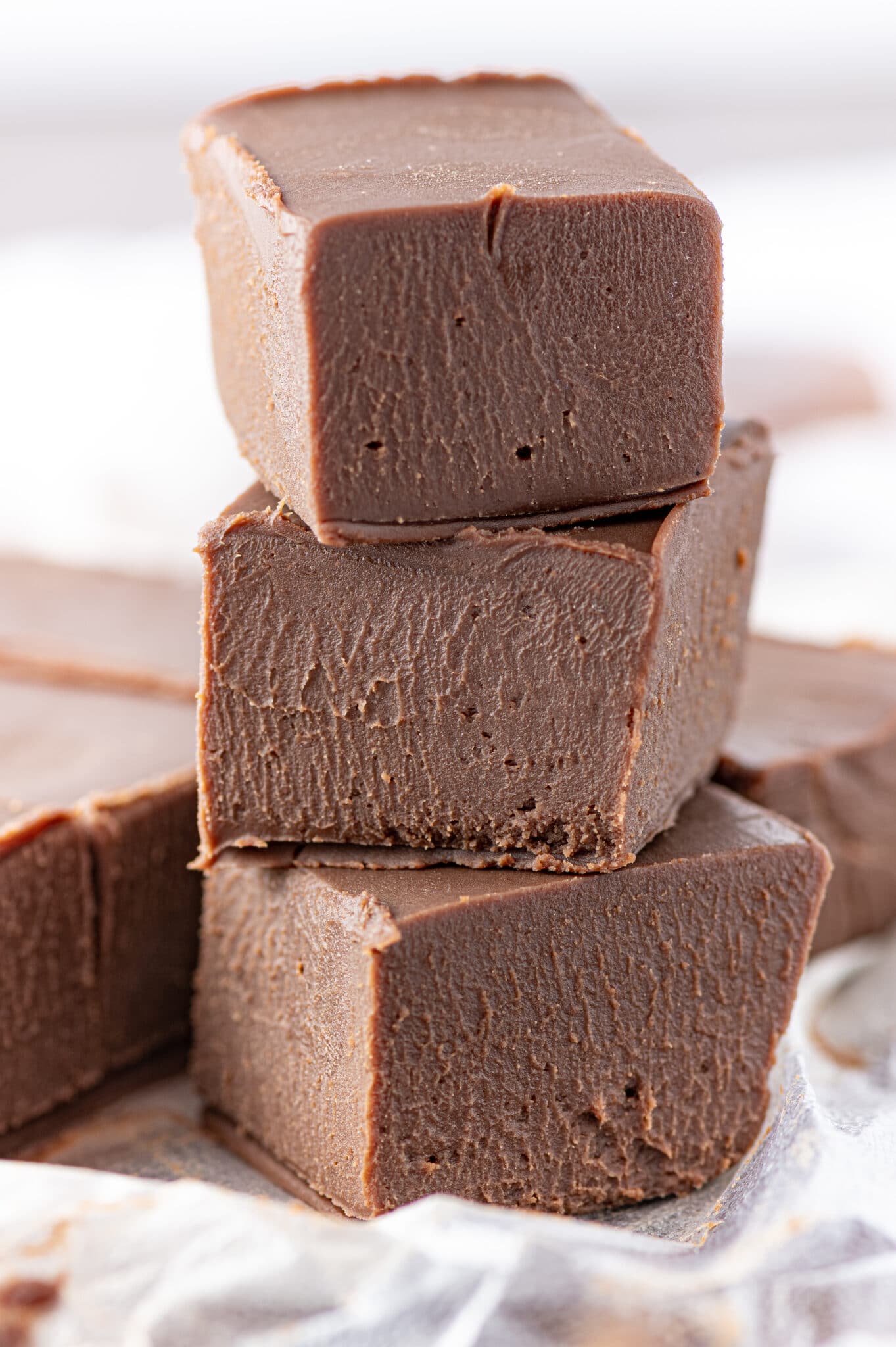 A stack of three pieces of chocolate keto fudge made with this recipe against a bright white background.
