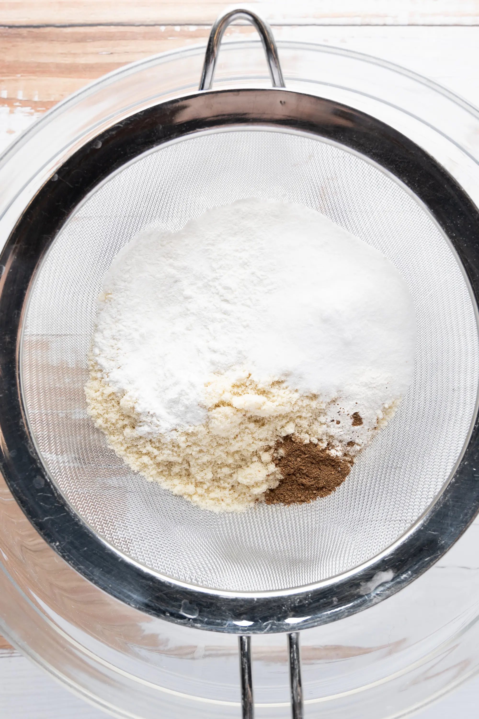 Low carb dry ingredients in a sifter sitting over a clear mixing bowl. 