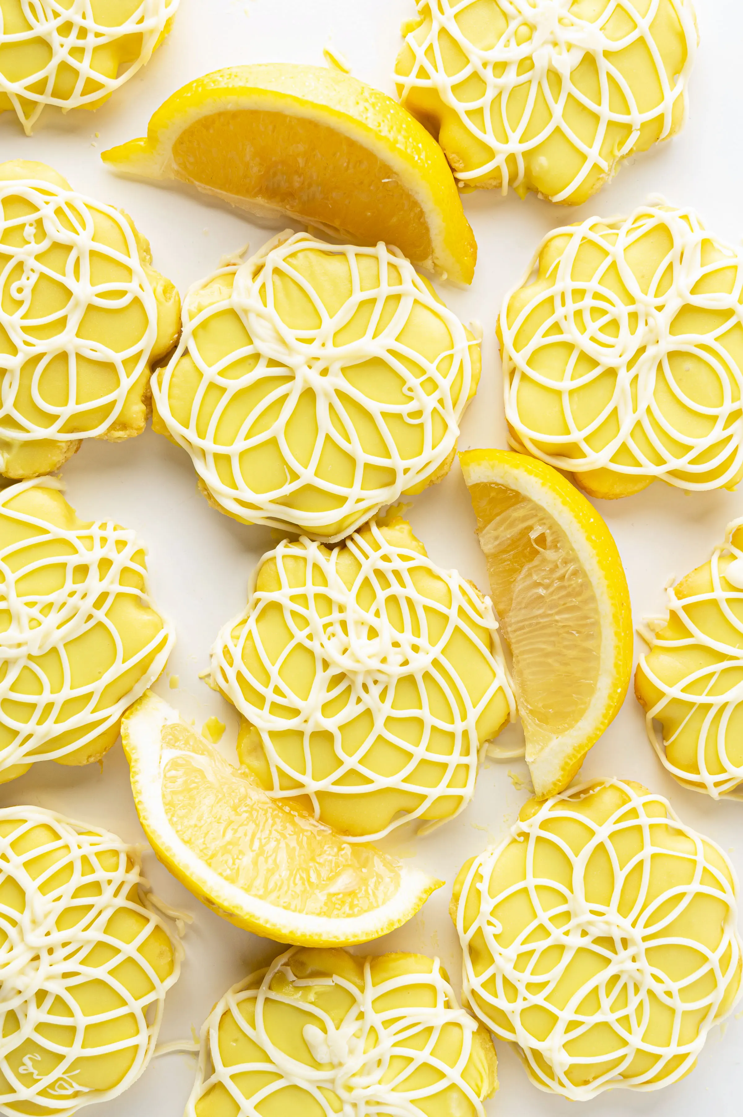 A tray of bright yellow lemon sugar cookies with white chocolate swirls with slices of fresh lemon. 