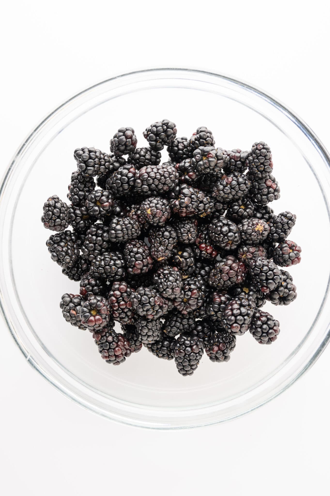 Bowl of fresh ripe blackberries against a bright white background.