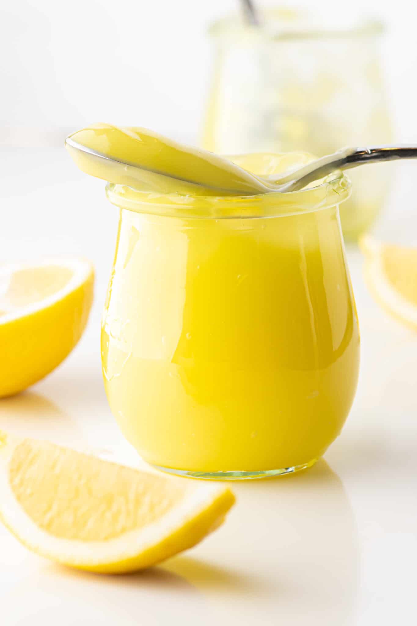 A jar of keto lemon curd with a filled spoon resting on top. 