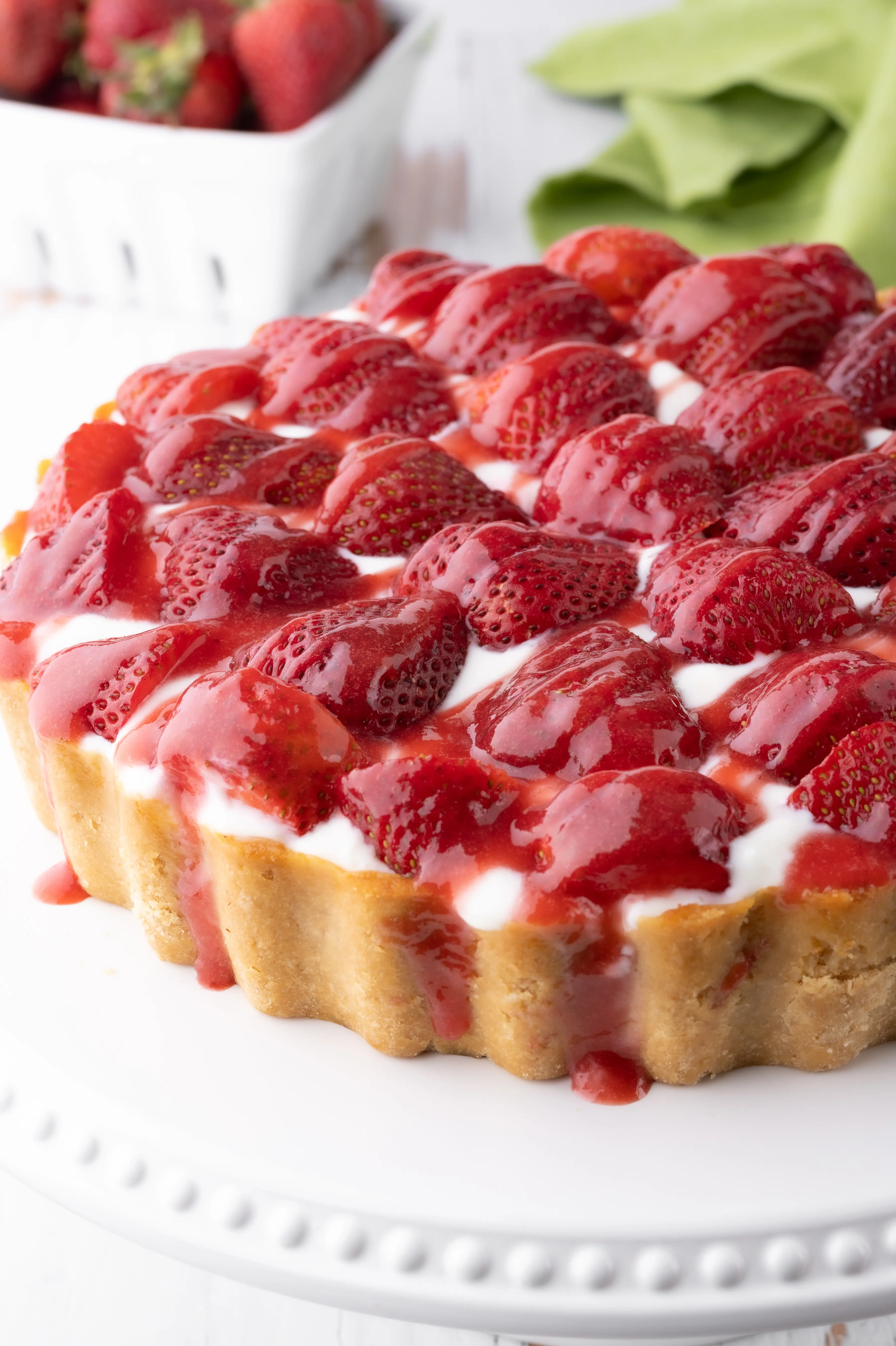 Keto strawberry cheesecake with fresh strawberries and drizzled with strawberry sauce.  The cheesecake rests on a bright white cake stand. 