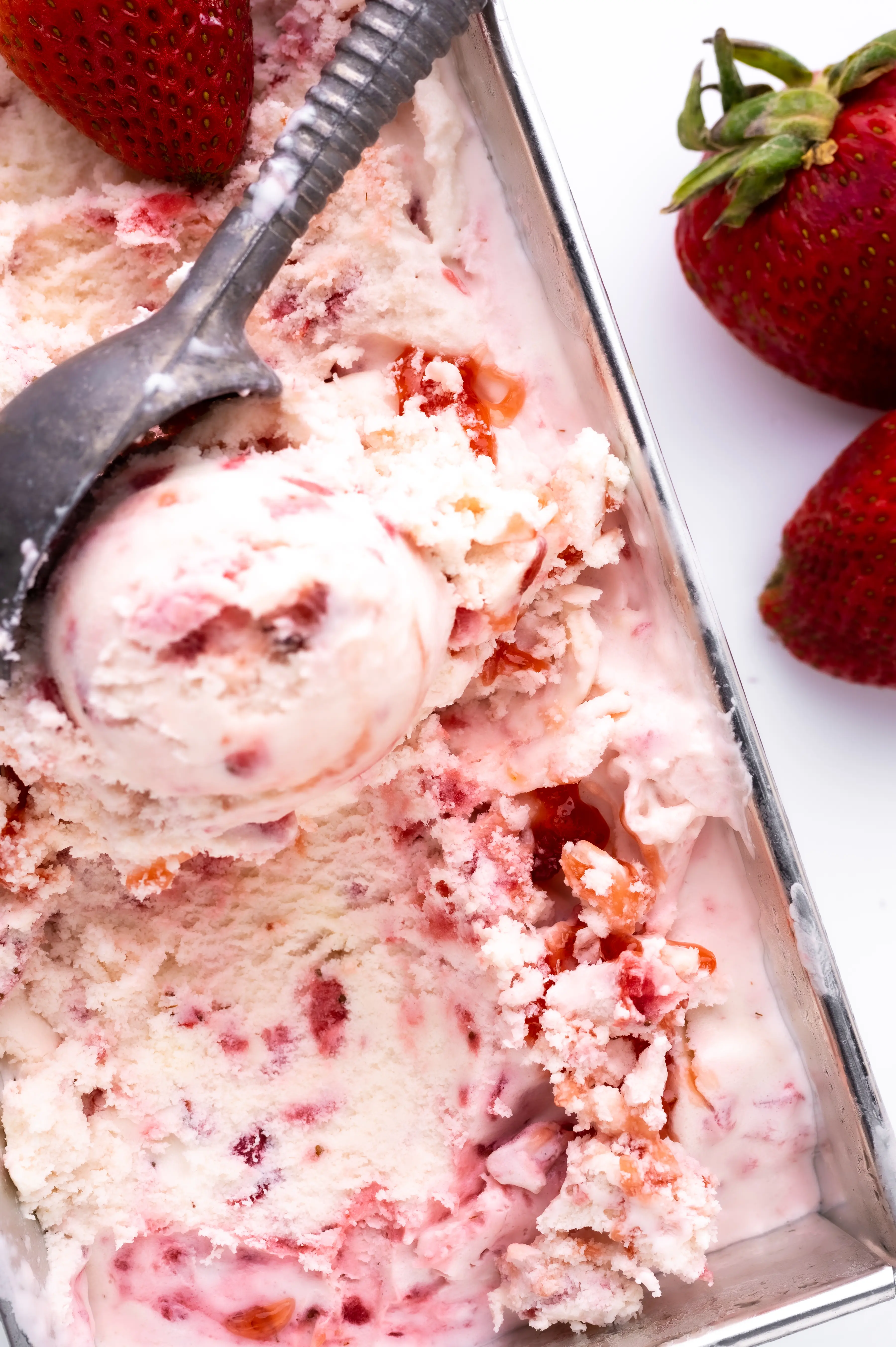 A pan of strawberry ice cream with an old fashioned ice cream scoop 