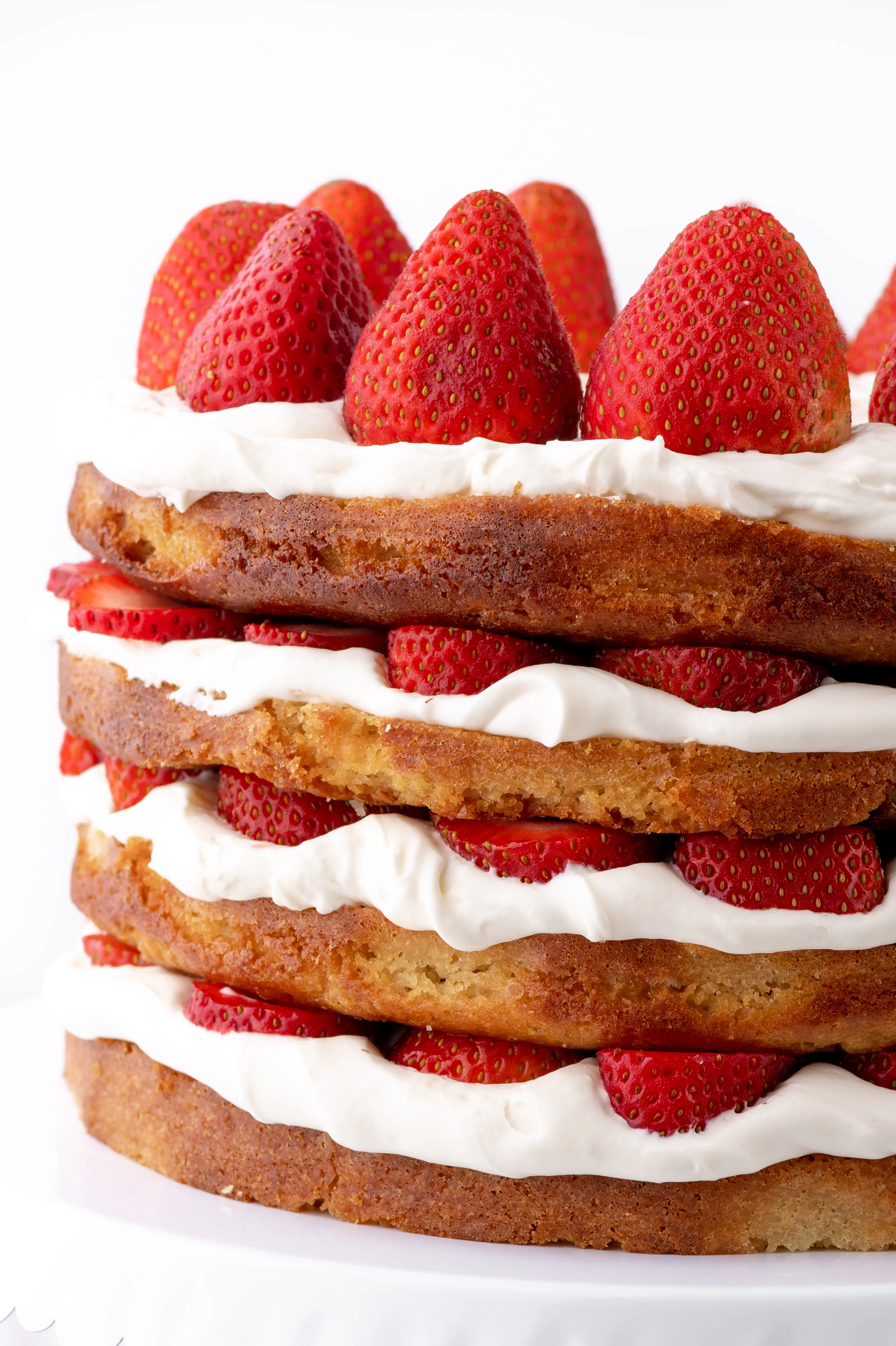 A four layer keto strawberry shortcake with fresh strawberries and whipped cream against a bright white background. 