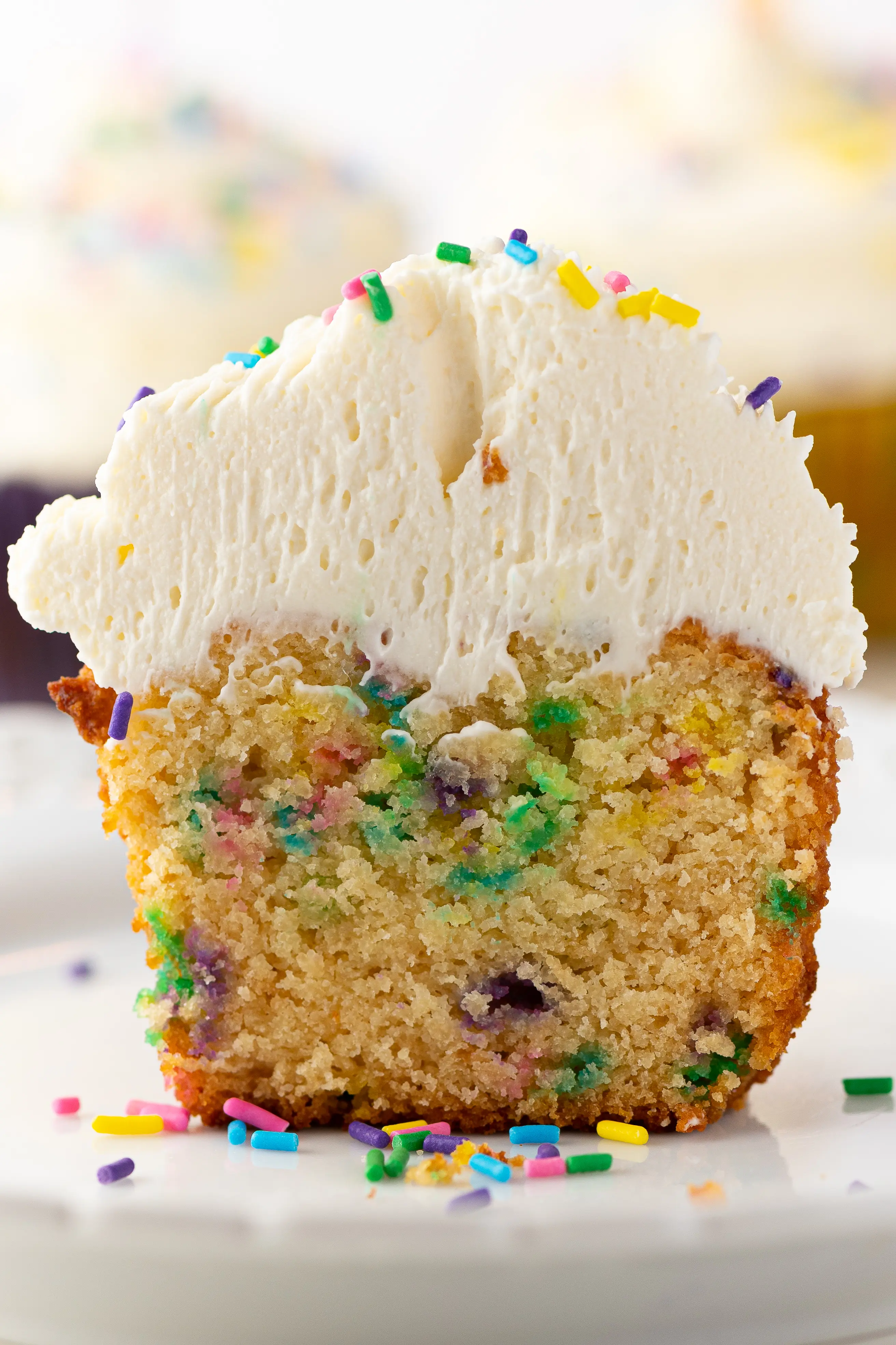 A birthday cupcake cut down the centre to show the inside.  The cupcake is topped with a mound of fresh white whipped cream frosting and colorful candy sprinkles.