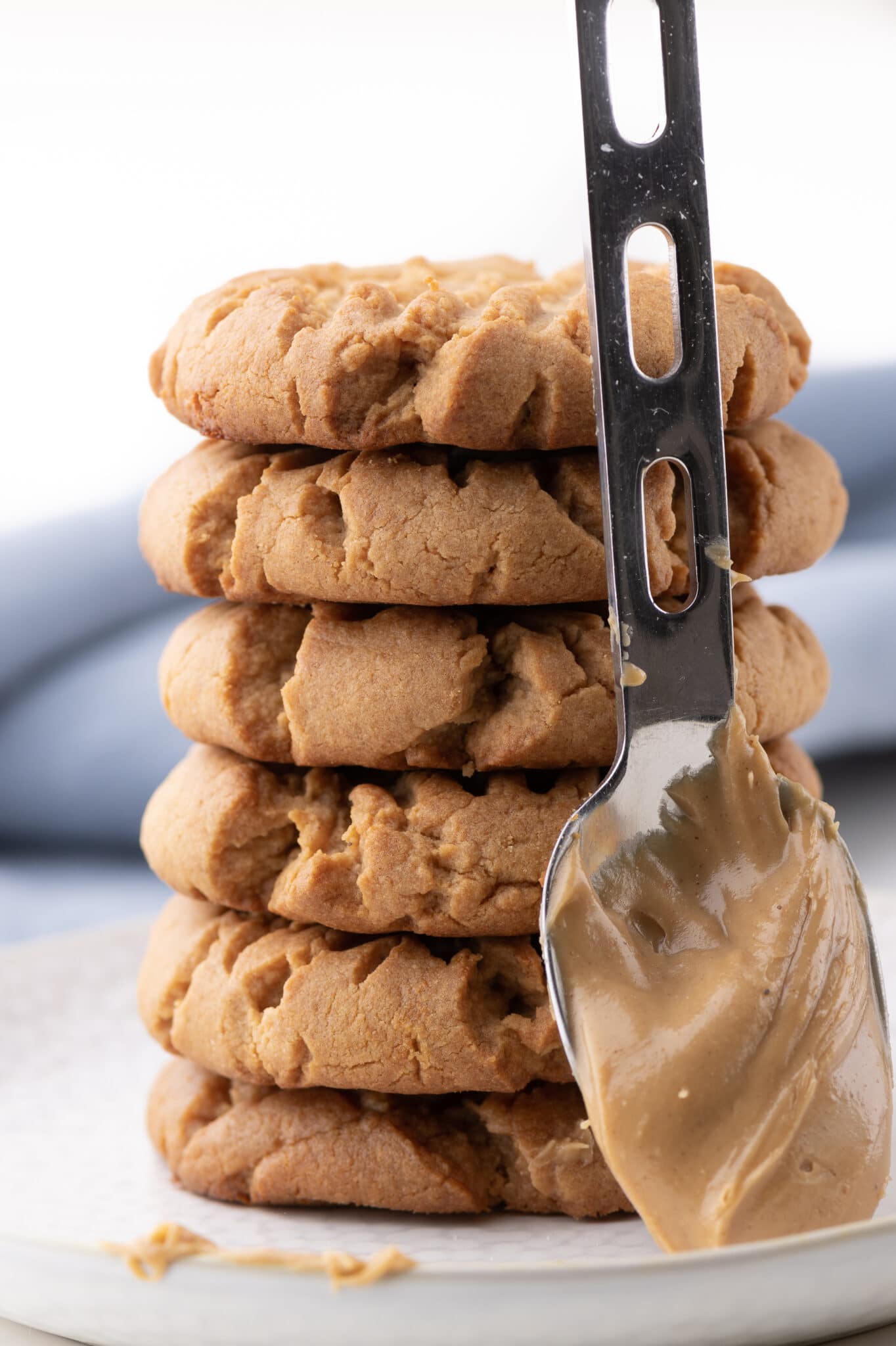 A stack of peanut butter keto cookies with a spoon coated in peanut butter sits in front. 
