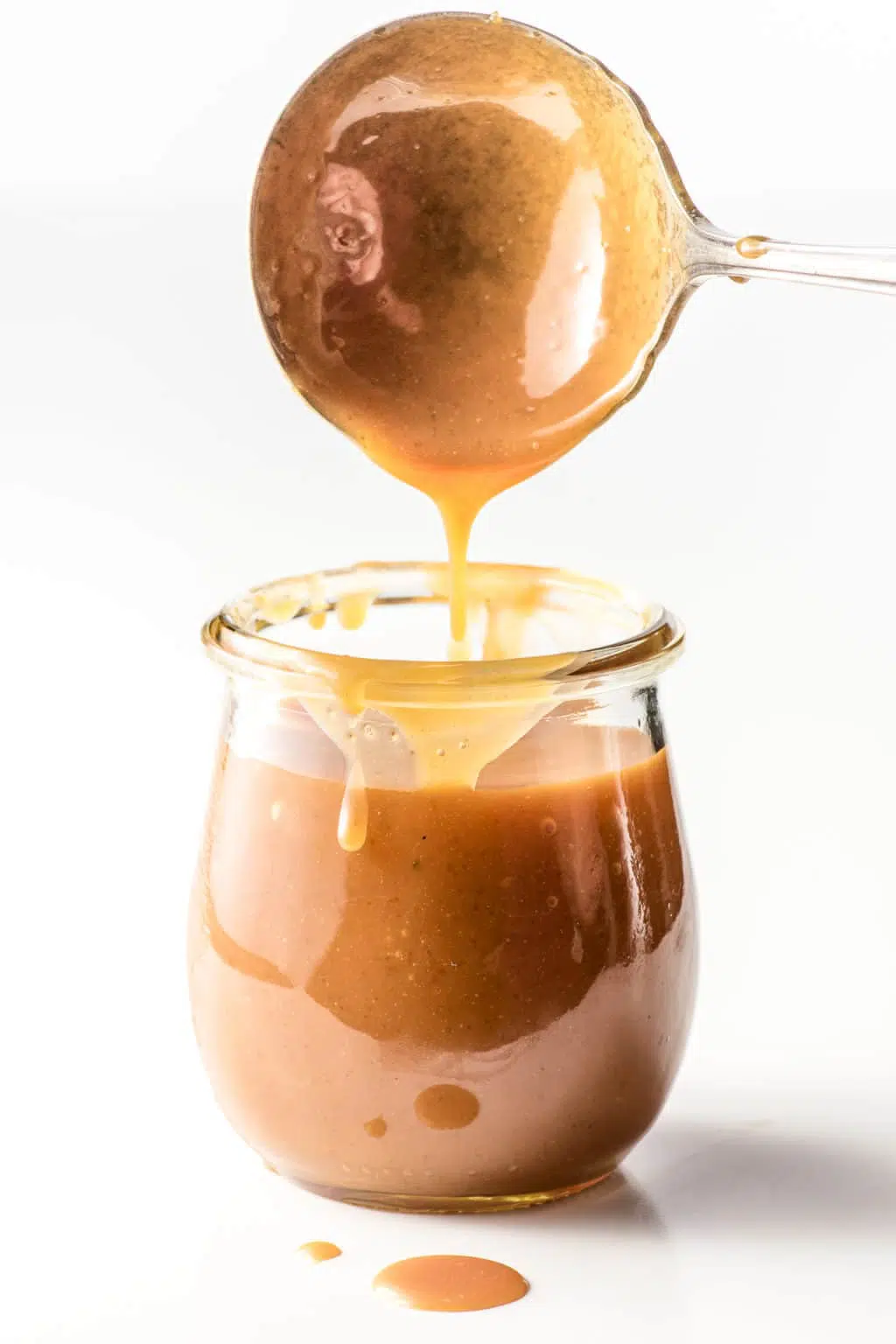 A spoon drizzling keto caramel into a small jar.