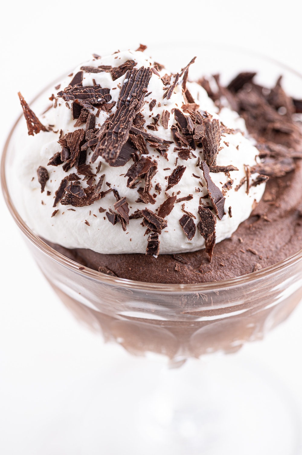 Sugar-free chocolate mousse in a glass dish with a dollop of whipped cream and dark chocolate shavings. 